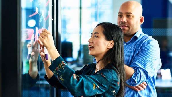  Two professionals looking at sticky notes on a glass wall