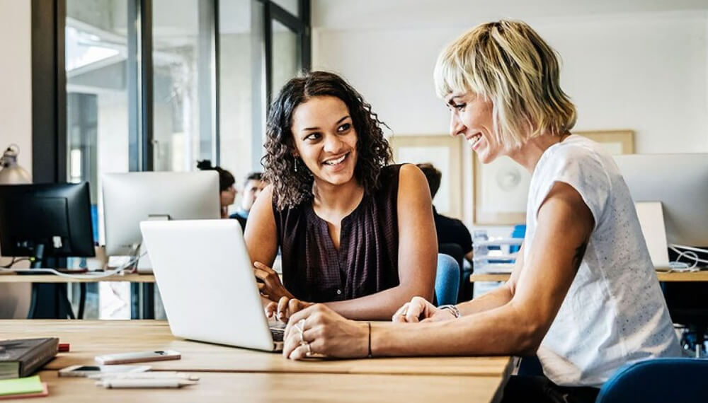 Female colleagues smiling in front of a laptop